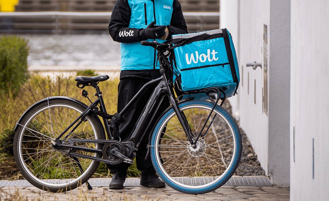 wolt dostavljač s biciklom i torbom za dostavu ispred ulaznih vrata kuće