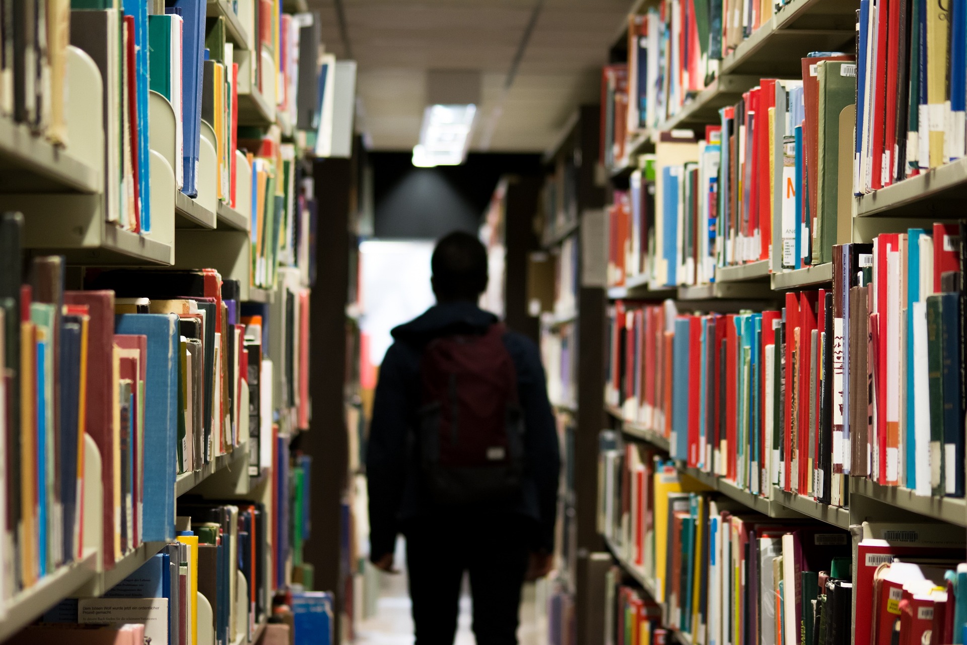 učenik s torob na leđima u redovima polica knjig au knjižnici okrenut leđima