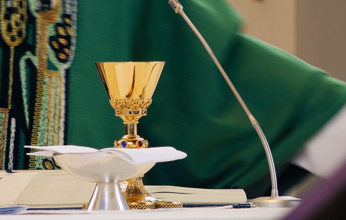 kalež na oltaru, u pozadini svećenik u zelenoj halji