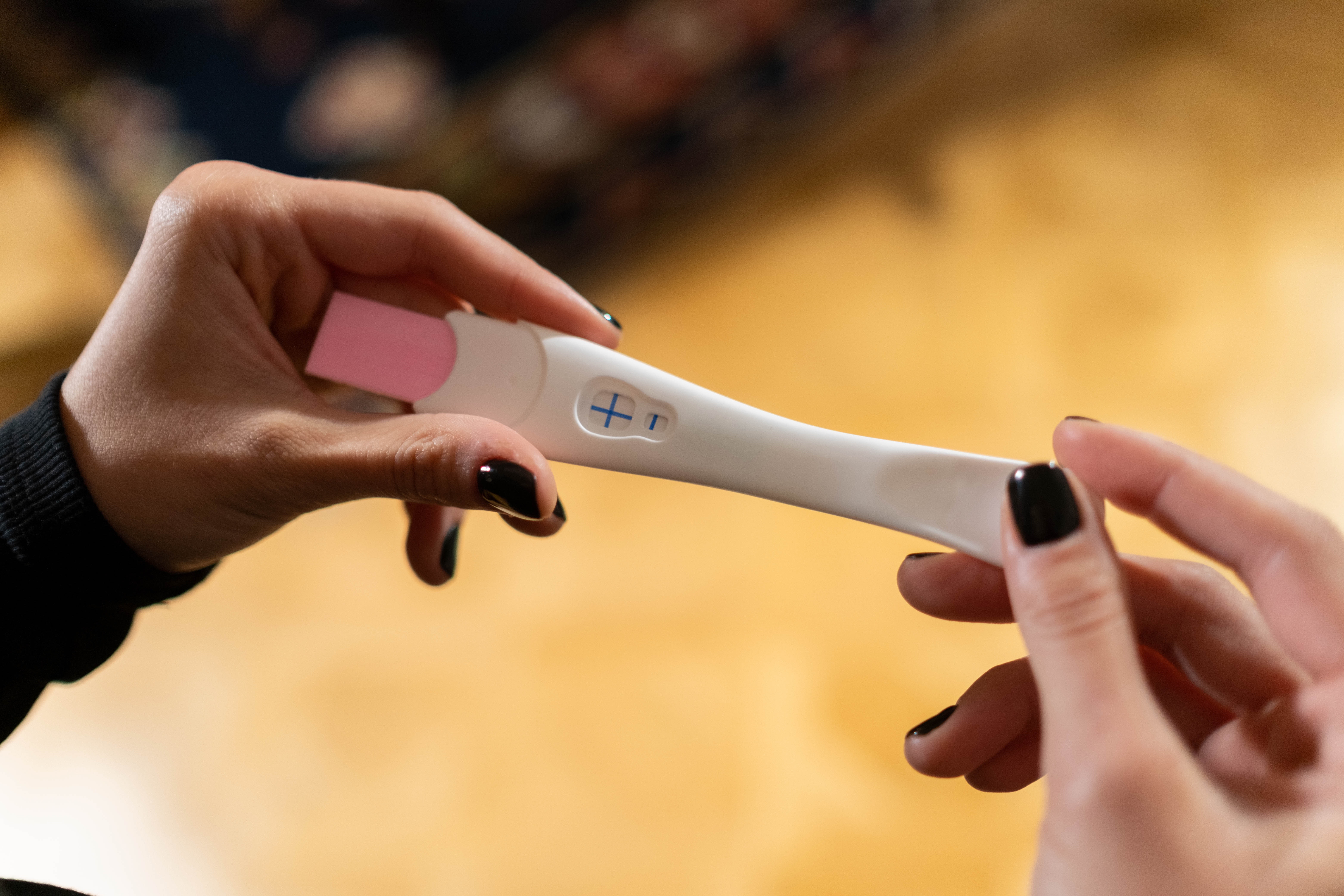 pozitivan test na trudnoću s plusićem u rukama djevojke koja ima nalakirane crne notke