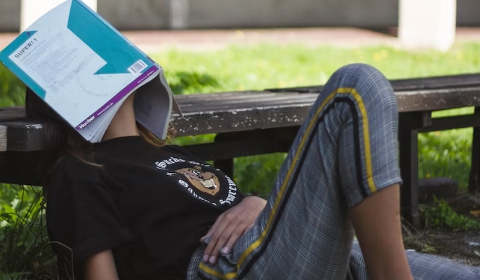 učenica leži u parku i ima knjigu na glavi