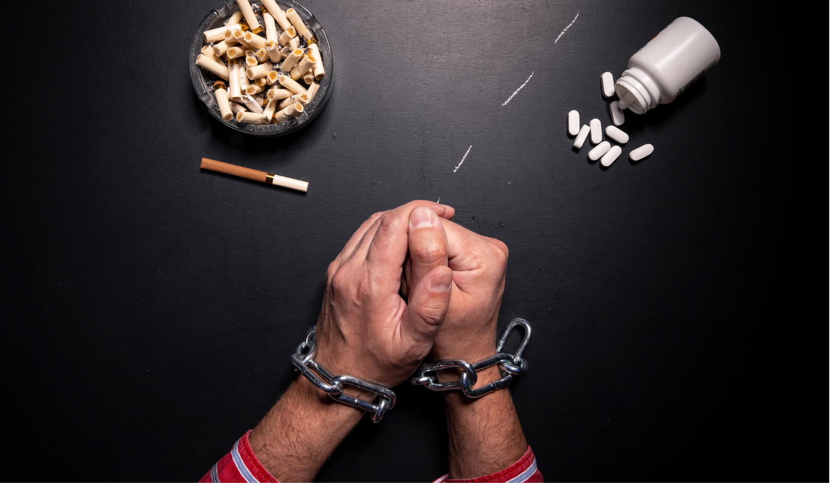 ovisnost, čovjek kojem su ruke vezane lancima, ispred njega su tablete i cigarete