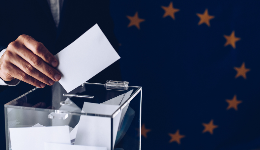 osoba koja stavlja glasački listić u kutiju, a u pozadini je zastava Europske unije