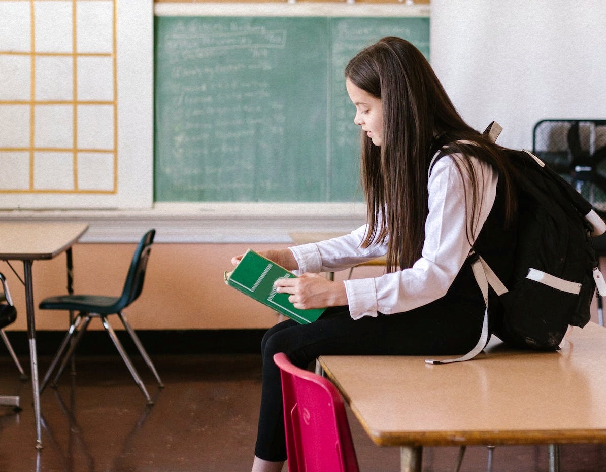 Učenica sjedi na klupi u učionici i čita knjigu