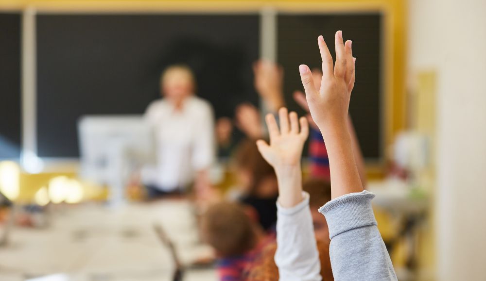 učenici drže rukeu zraku u učionici